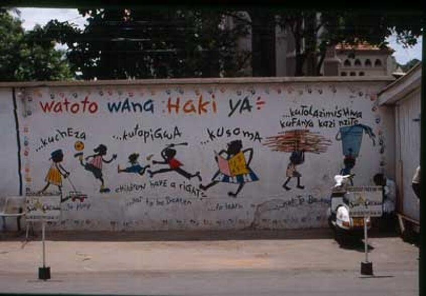 Auf der Wand sieht man bunte Bilder, in Farbe gezeichnet, spielende Kinder, Mädchen und Buben, eines hat ein Buch in der Hand, ein anderes läuft. Und darüber steht in Swahili: Watoto wana haki ya.